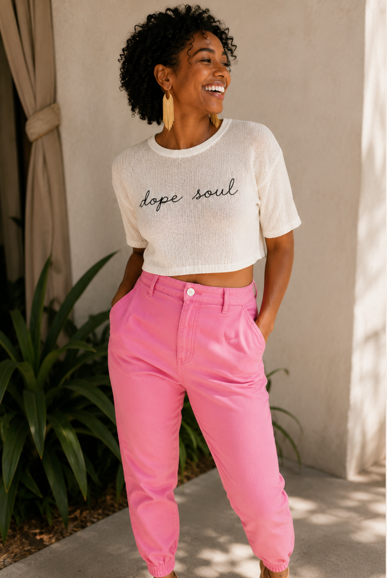Woman wearing a white 'dope soul' t-shirt and pink pants standing outdoors.