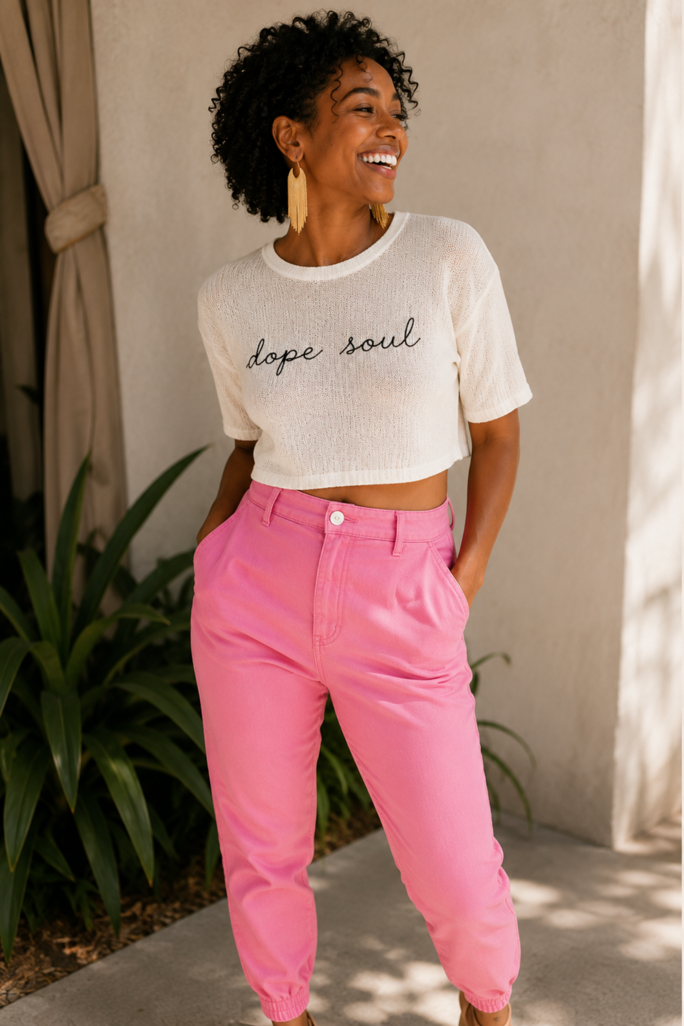 Woman wearing a white 'dope soul' t-shirt and pink pants standing outdoors.