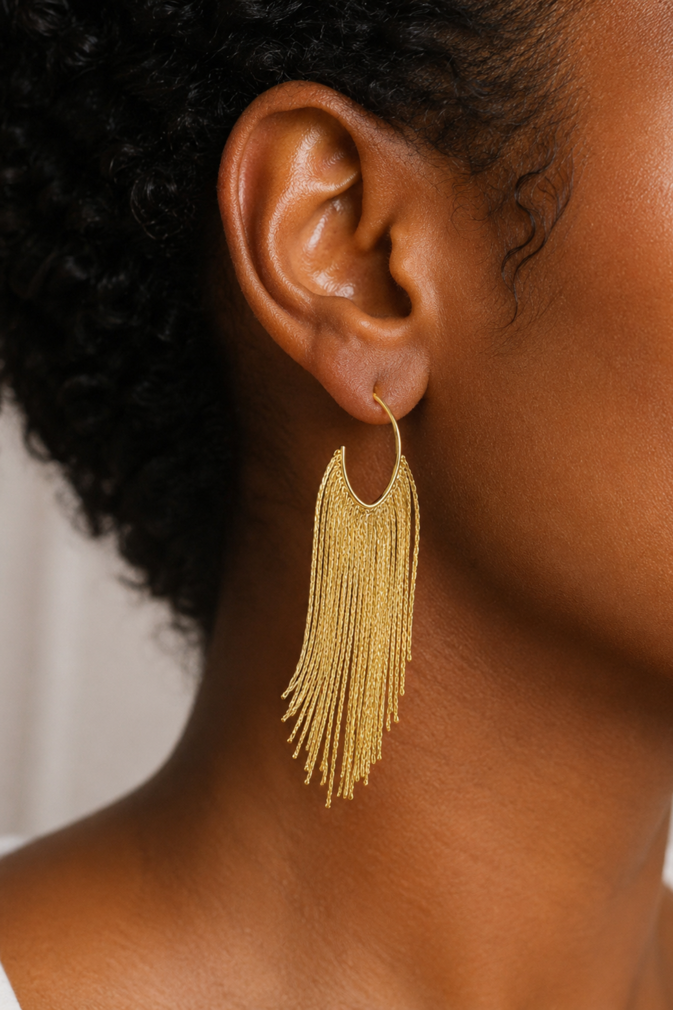 Gold fringe earring worn by a person with a neutral background