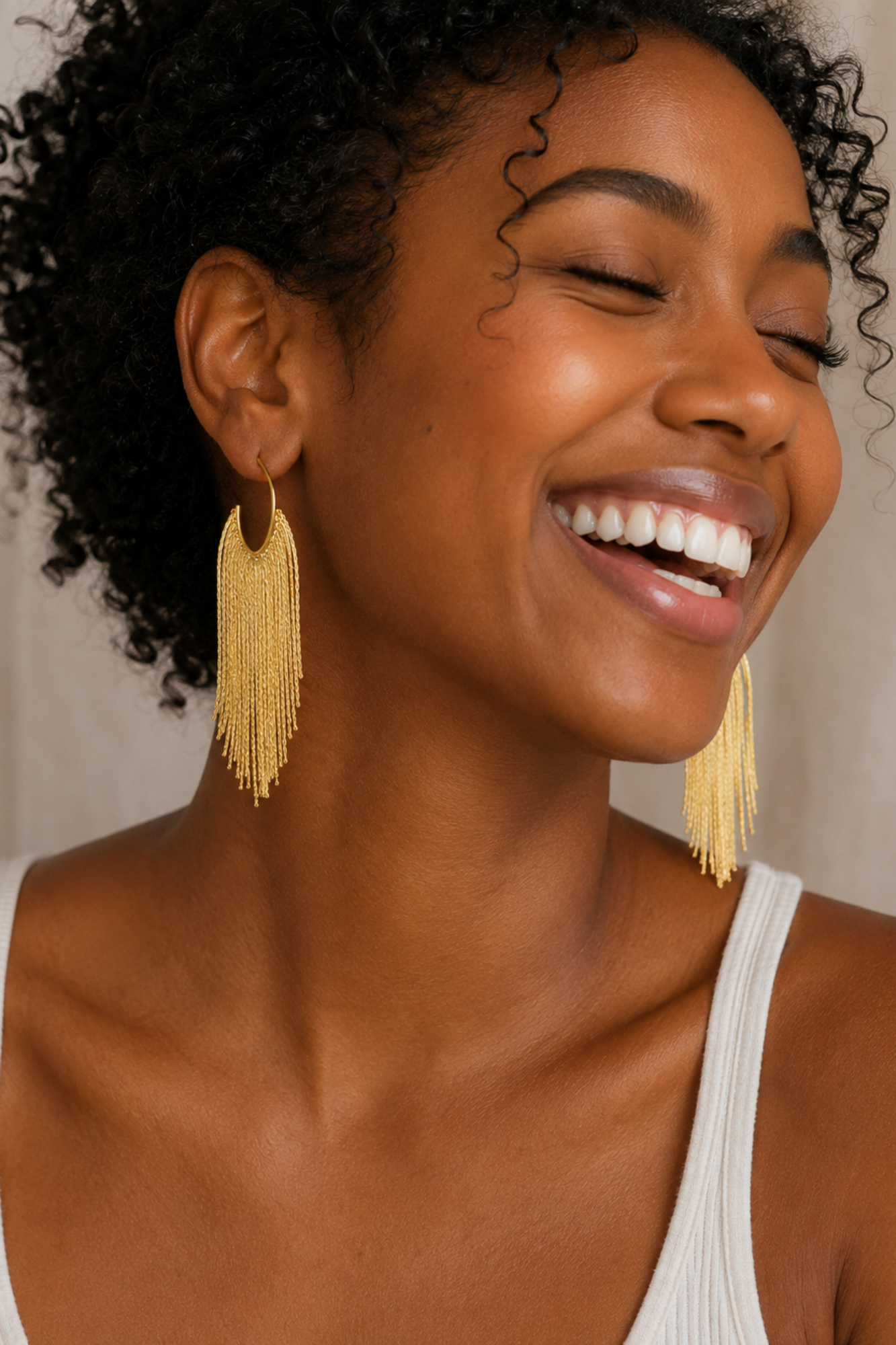 Woman wearing gold tassel earrings with a neutral background