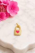 Gold lock-shaped pendant with a pink heart on a marble surface with pink flowers.