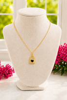 Gold necklace with a heart lock pendant on a mannequin bust with pink flowers in the background