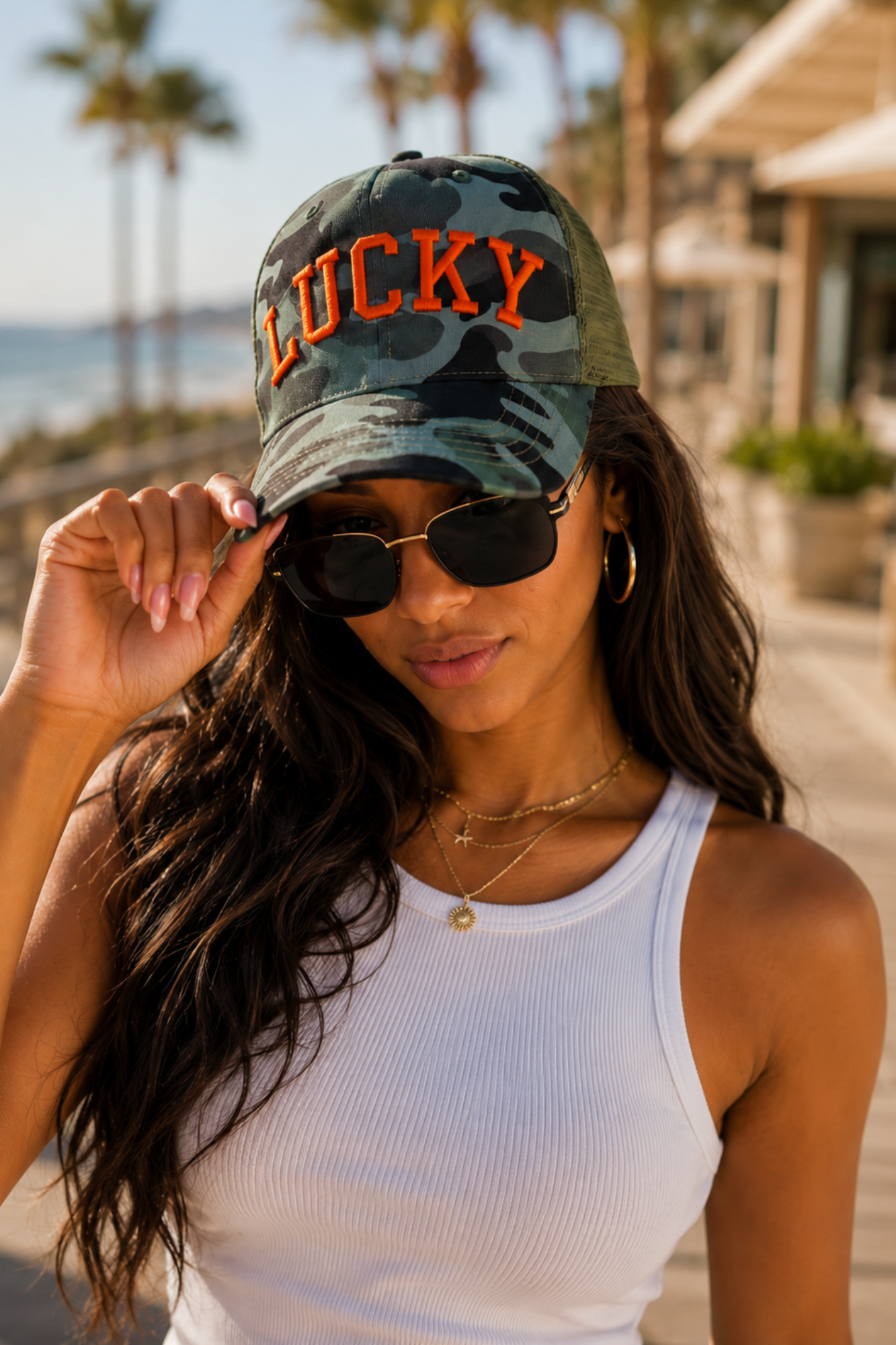 Woman wearing a cap with 'LUCKY' text and sunglasses outdoors.